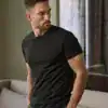 Man wearing a black stretch T-shirt, casual indoor setting.