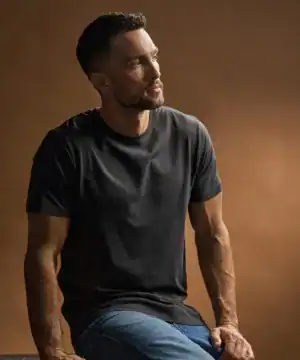 Man wearing a black luxury T-shirt, sitting against a brown background.