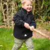 Child wearing a black PolarTherm jacket outdoors, smiling and playing with a stick.