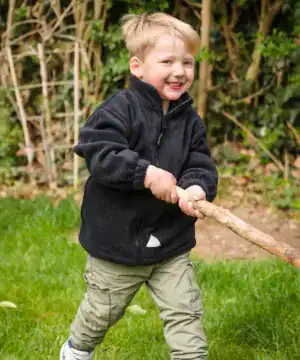 Child wearing a black PolarTherm jacket outdoors, smiling and playing with a stick.