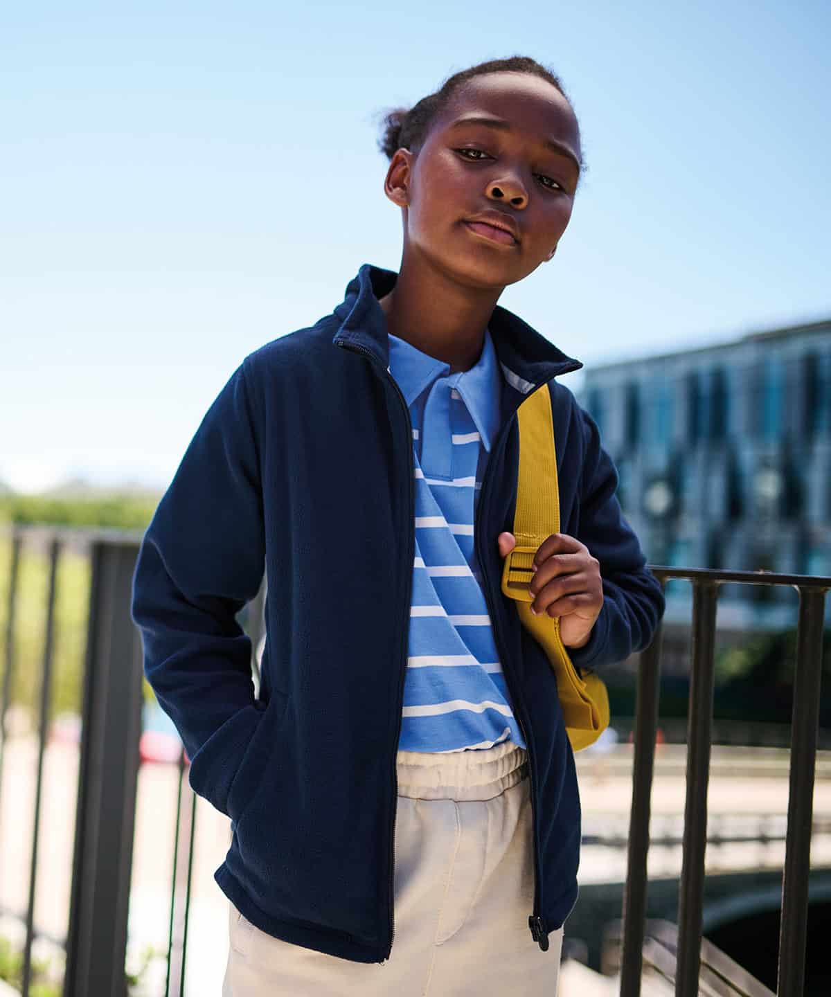 Child wearing school uniform with backpack outdoors.